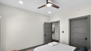 Ein Schlafzimmer mit einem Bett, einem Deckenventilator und zwei Türen.