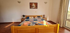 A bedroom with a wooden bed, a nightstand, a lamp, a painting on the wall, and a window with curtains. - 12 modern apartments for up to 4 people—each with its own kitchen and bathroom. (Ulcinj)