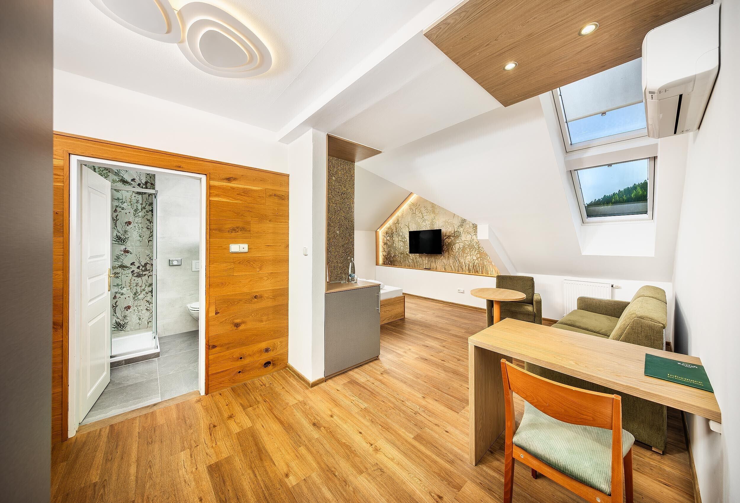 A modern interior with a wooden floor, a dining area with a table and chairs, a sofa, and a TV mounted on the wall.