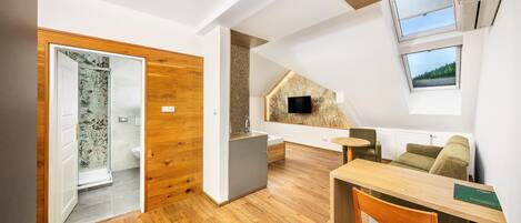 A modern interior with a wooden floor, a dining area with a table and chairs, a sofa, and a TV mounted on the wall.