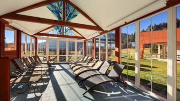 A sunroom with large windows, a ceiling with wooden beams, and lounge chairs arranged for sunbathing.