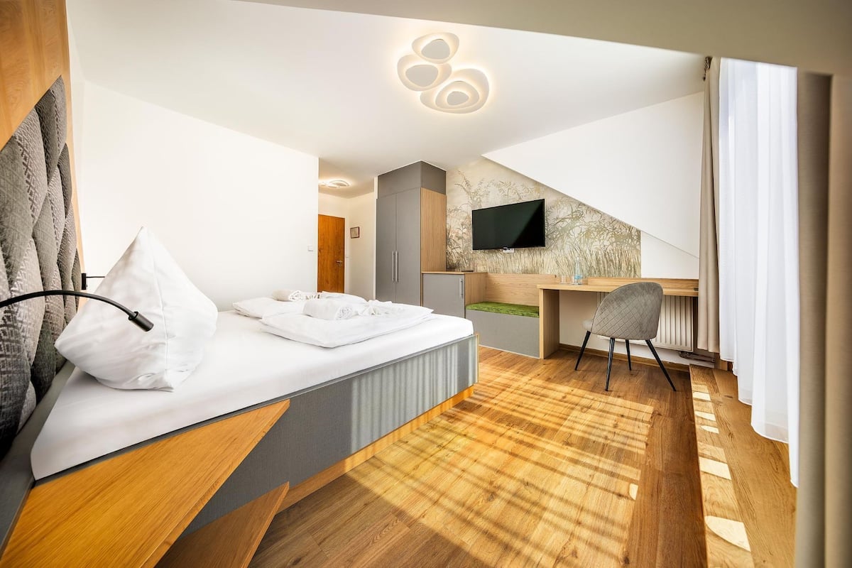 A modern hotel room with a bed, a desk, a chair, and a TV mounted on the wall.