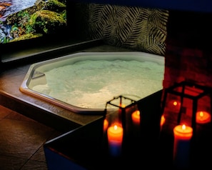 Una bañera con una fuente de agua verdosa, un papel tapiz estampado y velas.