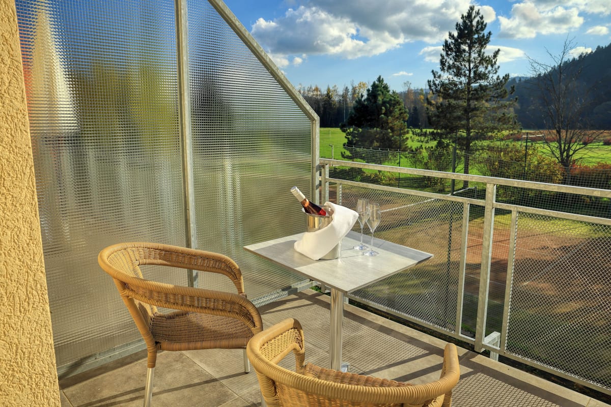 A balcony with wicker chairs, a table, and a bottle of wine.