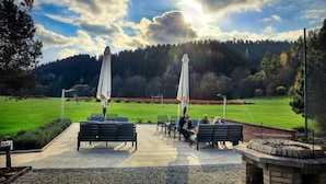 Un espace extérieur aménagé avec des tables et des chaises, des parasols et une vue sur une colline boisée.