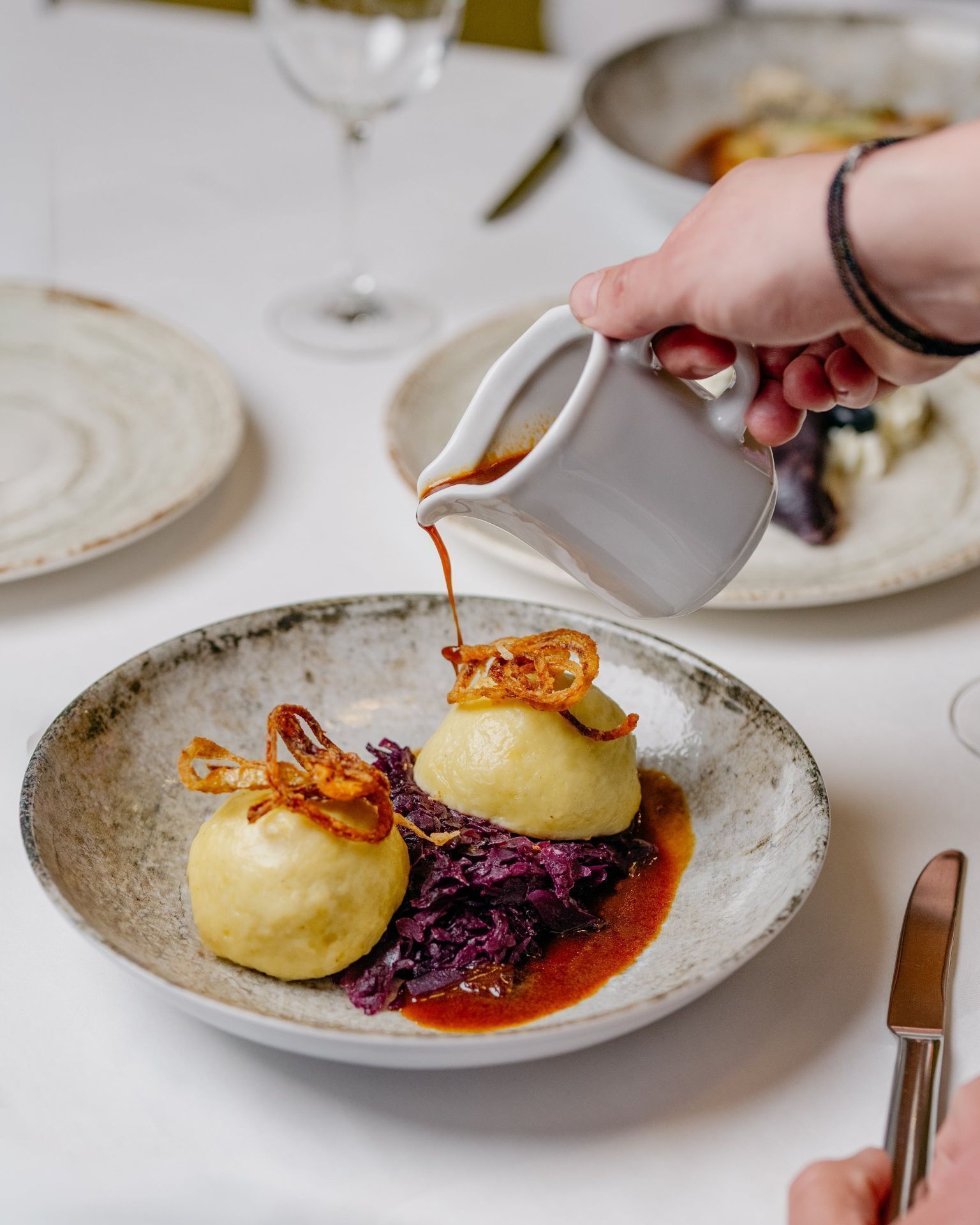 A plate with dumplings, red cabbage, and a sauce being poured over them.