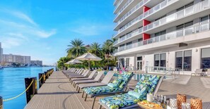 A poolside area with lounge chairs, umbrellas, and a dining setup. - Stylish Studio w/ Balcony, Gym & Shuttle (Hallandale Beach)