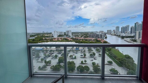 Blick von einem Balkon auf einen Fluss mit Gebäuden und einem Parkplatz.