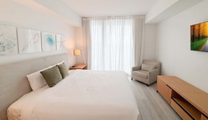 A hotel room with a large bed, a chair, a nightstand, and a painting on the wall. - Modern 1BR - Bay View  - Resort Amenities & Pool (Hallandale Beach)