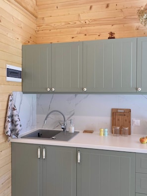 A kitchen with grey cabinets, a marble backsplash, a sink with a faucet, and a wooden cutting board. - Tiny House Wrzosowisko (Prościeniec)