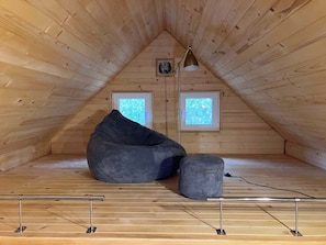 An attic room with wooden walls, a bean bag, a small table, and two windows. - Tiny House Wrzosowisko (Prościeniec)