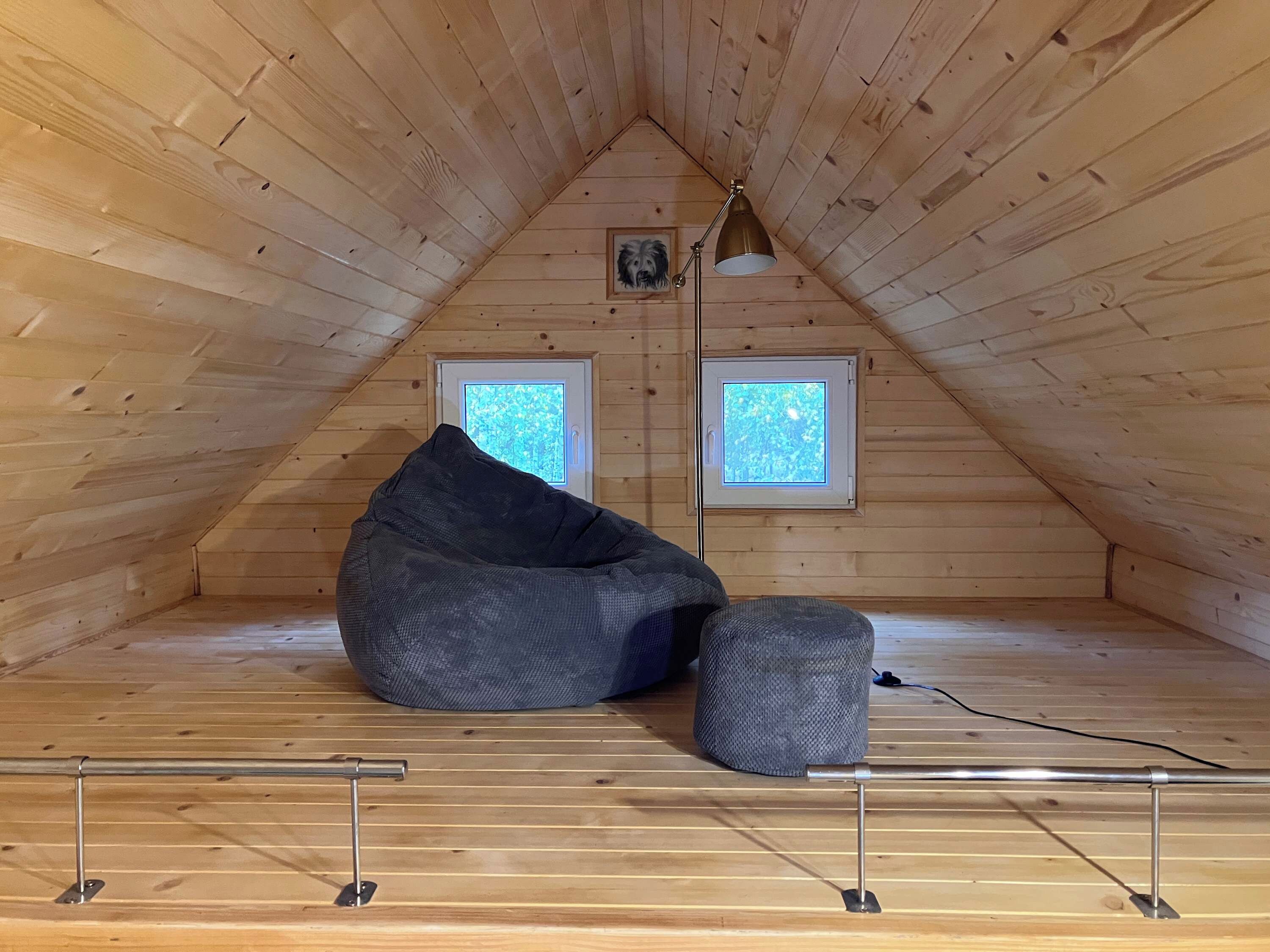 Ein Dachzimmer mit Holzwänden, einem Sitzsack, einem kleinen Tisch und zwei Fenstern.