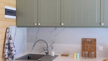 A kitchen with grey cabinets, a marble backsplash, a sink with a modern faucet, and a wooden cutting board.