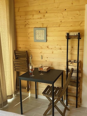 A wooden interior with a table, chairs, a wine bottle, glasses, and a framed picture on the wall.