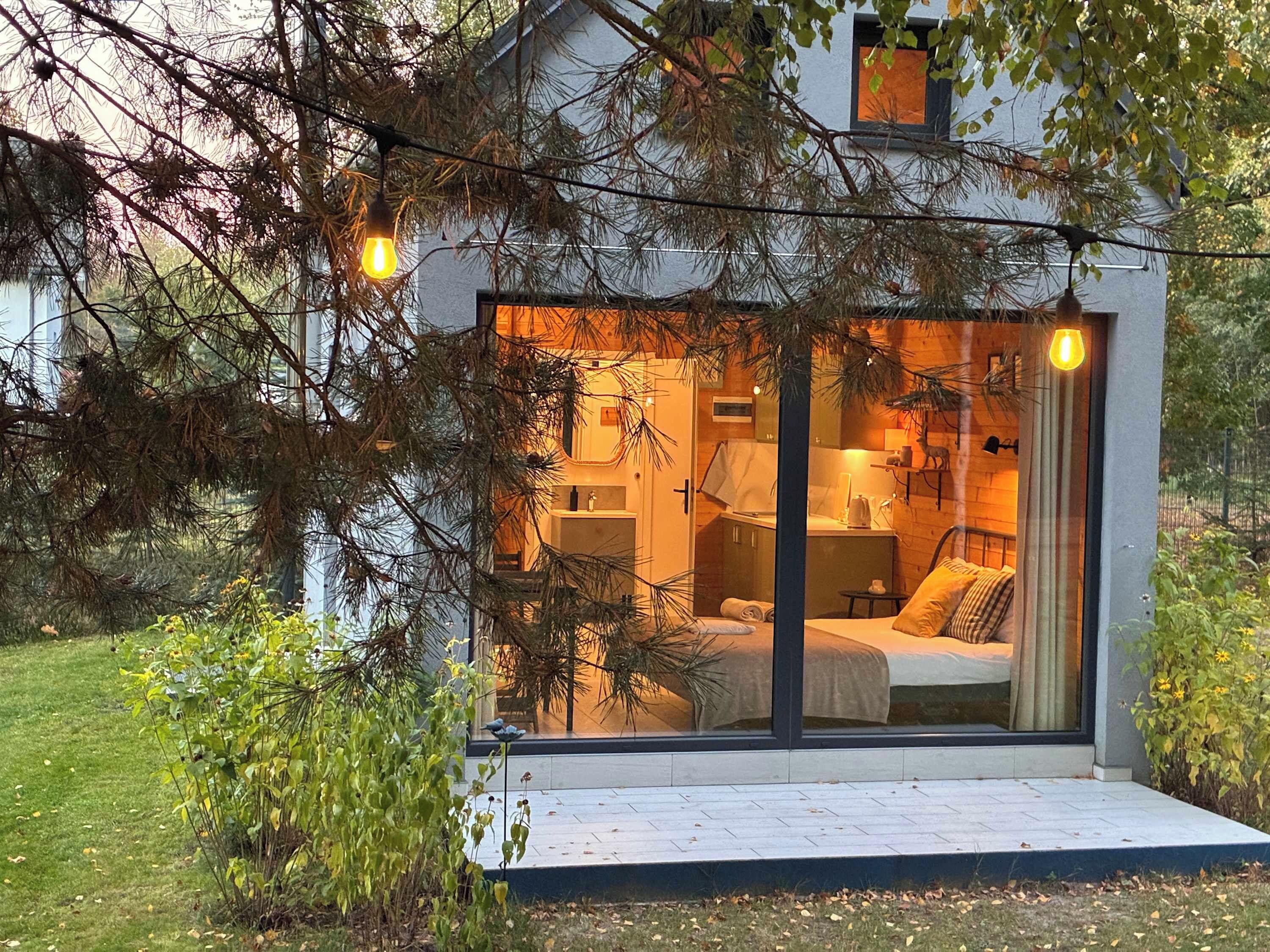 Una cabaña moderna con fachada de vidrio, una cama y una pequeña cocina.