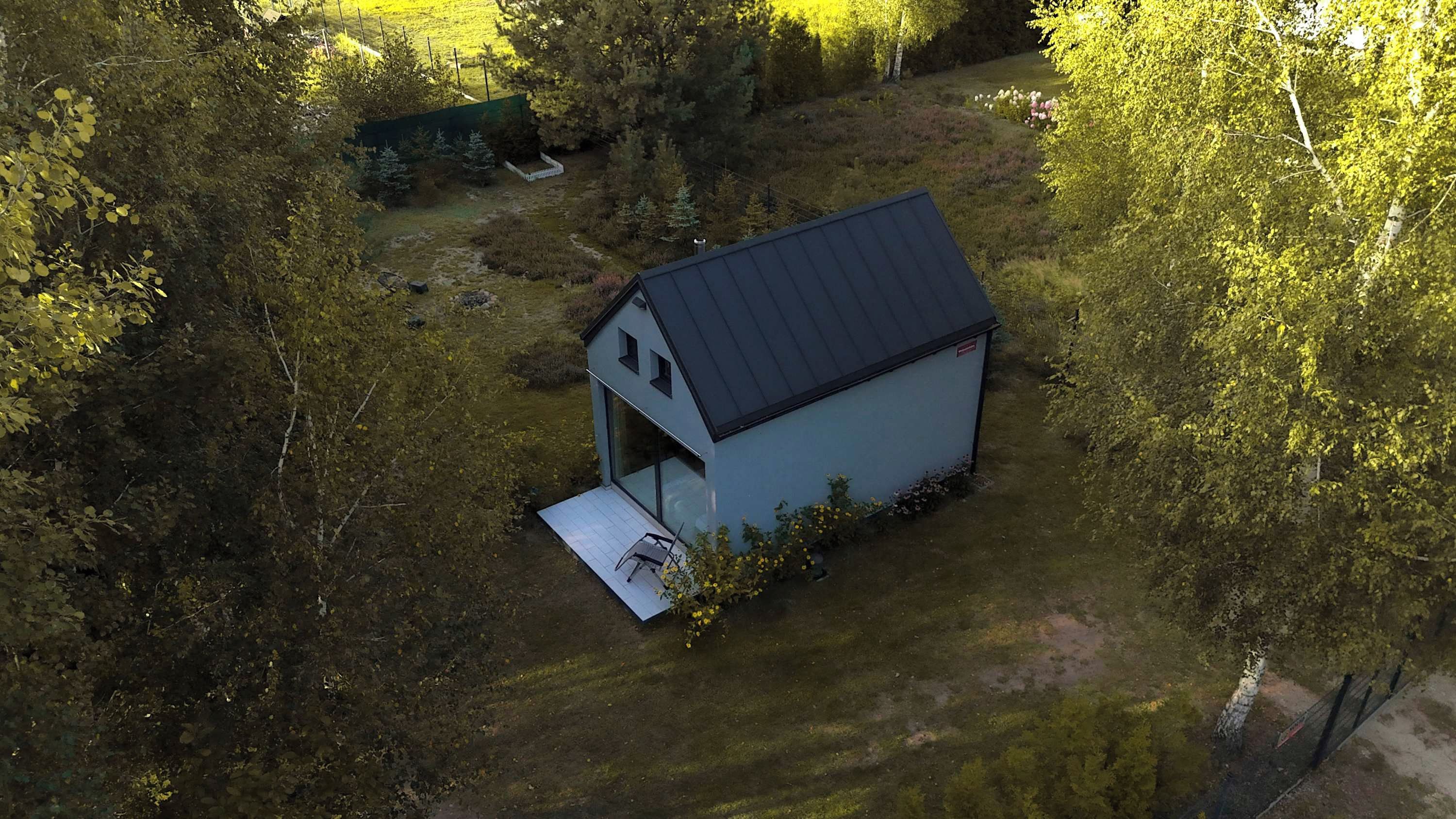 Uma casa térrea com telhado escuro, cercada por árvores densas e um gramado.
