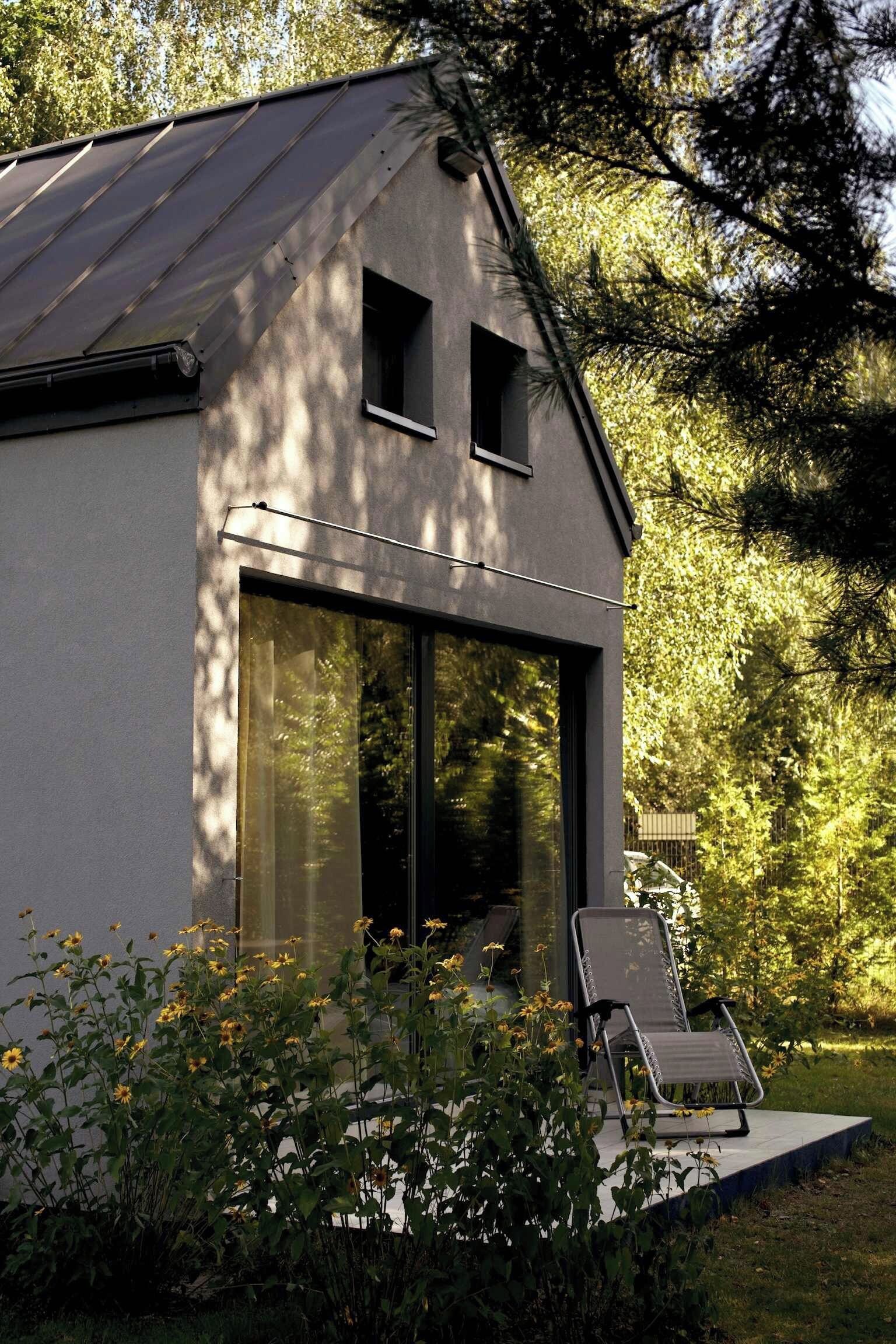 Uma casa moderna com uma grande janela de vidro, telhado metálico e um jardim florido.