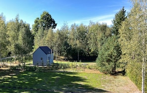 A small white building with a dark roof, surrounded by a fenced yard and dense trees. - Tiny House Wrzosowisko (Prościeniec)