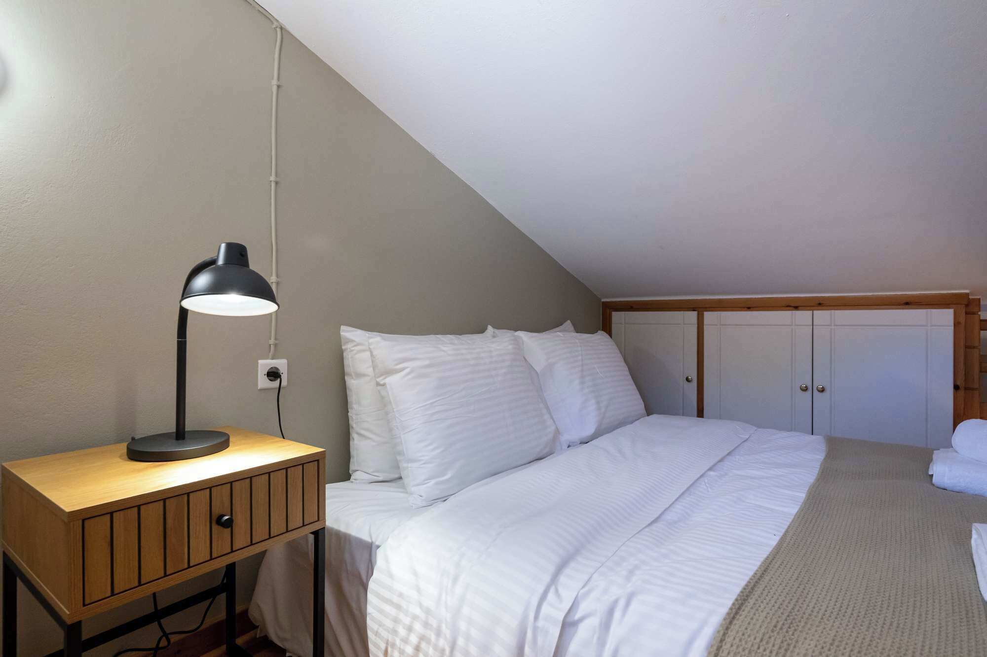 Een slaapkamer met een bed, een bureau met lamp en een kledingkast.