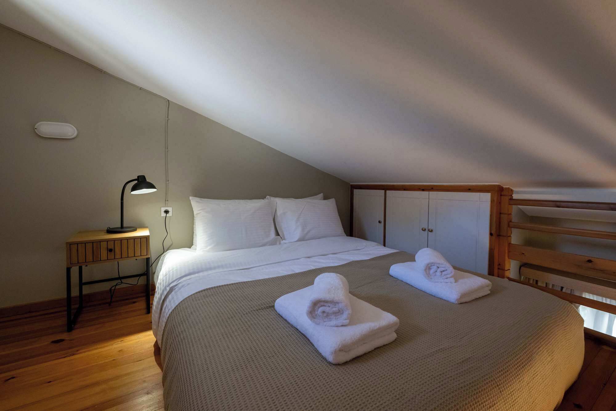 A bedroom with a bed, bedside lamp, wooden floor, and a bunk bed in the corner.