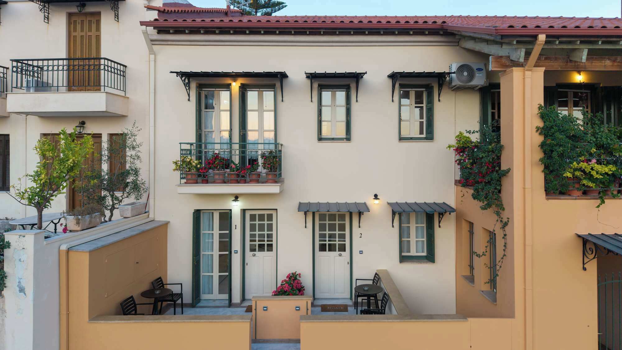 A two-story building with a balcony, a small outdoor seating area, and a door marked with the number 1.