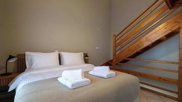 A bedroom with a bed, two pillows, a bedside lamp, a wooden staircase, and a small table.