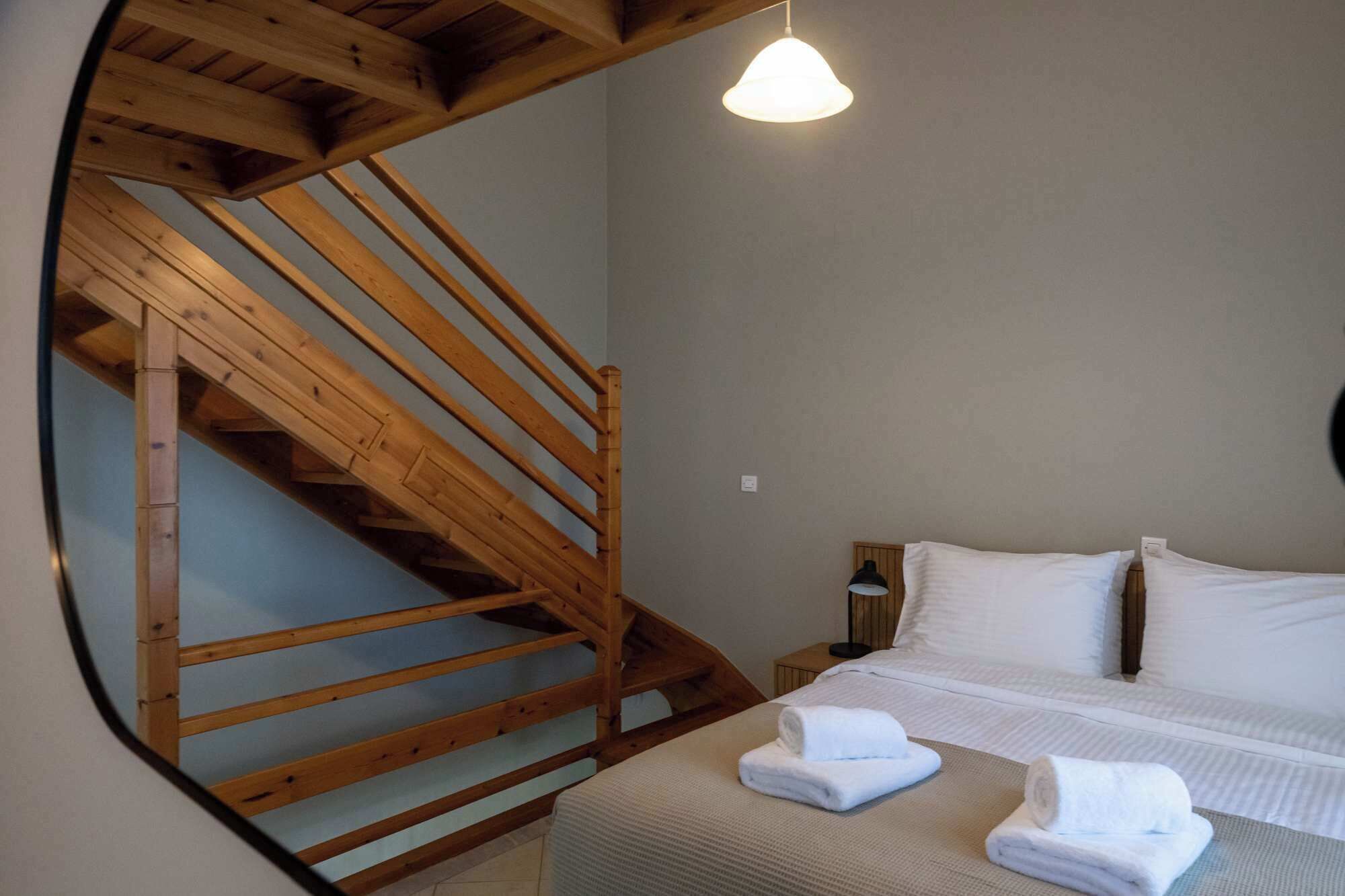 Un dormitorio con una escalera de madera, una cama con ropa de cama blanca y una lámpara de noche.