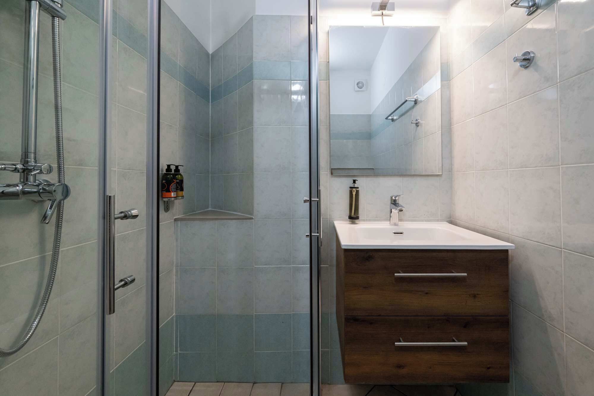 A bathroom with a glass shower enclosure, a wooden vanity with a sink, and a mirror above the vanity.