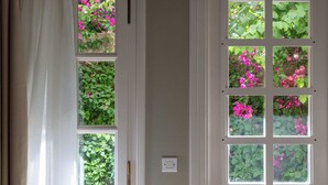 A room with a large window divided into multiple panes, each with a view of greenery and pink flowers. - Ipapanti Square (Kalamata)