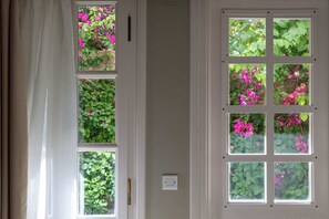 Una habitación con un ventanal grande dividido en varios paneles, cada uno con vistas a follaje y flores rosadas.