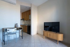 Um espaço de estar compacto com cozinha compacta, área de jantar com mesa e cadeiras e uma televisão sobre um armário de madeira.