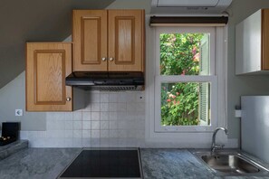 A kitchen with wooden cabinets, a stainless steel sink, and a window with a view of greenery. - Ipapanti Square (Kalamata)