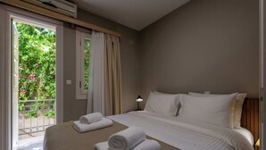 A hotel room with a bed, two towels, a nightstand, a lamp, and a window with curtains. - Ipapanti Square (Kalamata)