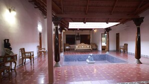 A spacious indoor area with a tiled floor, wooden furniture, and a central decorative pool. - N D Farms (Kanakapura)