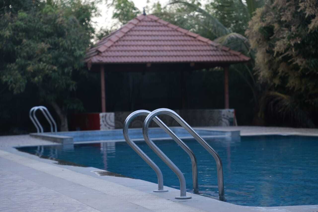Una piscina con barandillas de metal, una estructura de techo con tejas y follaje circundante.
