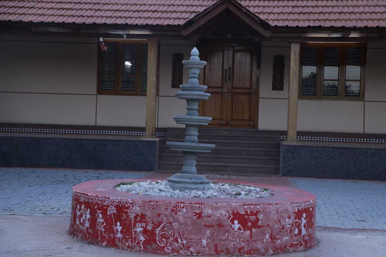 Eine Steinfontäne mit kreisförmigem Sockel, ein Gebäude mit einem Ziegeldach und Holztüren sowie ein befestigter Ziegelplatz.
