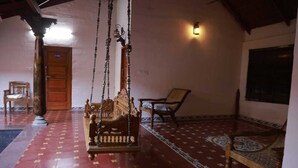 A room with a swing chair, a wooden door, a patterned floor, and a wall-mounted light fixture. - N D Farms (Kanakapura)