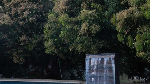 A swimming pool with a waterfall feature and lush greenery in the background. - N D Farms (Kanakapura)
