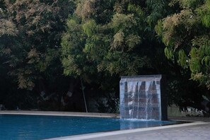 A swimming pool with a waterfall feature and lush greenery in the background. - N D Farms (Kanakapura)