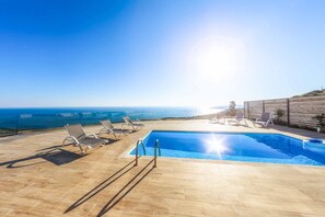 Ein Pool mit Liegestühlen, einer Holzterrasse und Blick auf das Meer.