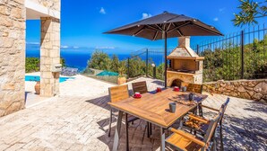 An outdoor patio with a stone table, chairs, and a barbecue grill. - Sunset Vista Villas Deluxe III (Zakynthos)