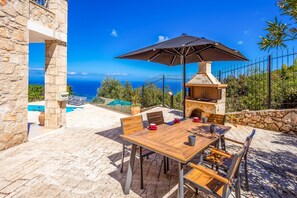 Eine Terrasse im Freien mit einem Steintisch, Stühlen und einem Grill.