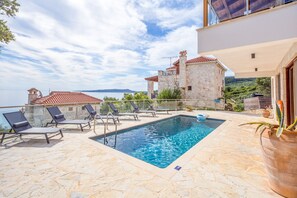 Ein Swimmingpool mit Liegestühlen, ein Steinhaus und Meerblick.