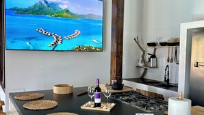 A kitchen with a large island, a television displaying a scenic view, and various kitchen items. - Boho Villa in Firgas | Pool, Nature, BBQ, and Ocean Views (CN)