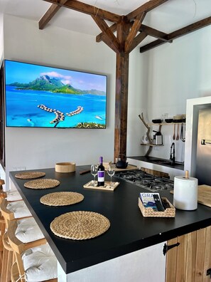 Eine Küche mit einer großen Kochinsel, einem Fernseher, der eine schöne Aussicht zeigt, und verschiedenen Küchenutensilien.