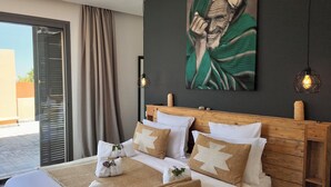 A hotel room with a bed, a wooden headboard, a large painting, and a view through a sliding door. - Villa Loulou, heated pool and breakfast included (Marrakech)