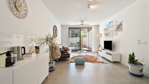 A modern living room with a sofa, coffee table, TV, and a large clock on the wall. - Family Oasis: Vacation rental with a 140 m² terrace, pool, and just 5 minutes from the beach (AN)