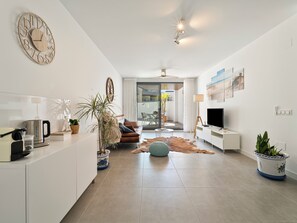A modern living room with a sofa, coffee table, TV, and a large clock on the wall. - Family Oasis: Vacation rental with a 140 m² terrace, pool, and just 5 minutes from the beach (AN)