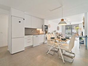 A modern kitchen with white cabinetry, a glass dining table, and a hanging pendant light. - Family Oasis: Vacation rental with a 140 m² terrace, pool, and just 5 minutes from the beach (AN)