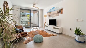 A modern living room with a flat-screen TV, leather sofa, and a large window. - Family Oasis: Vacation rental with a 140 m² terrace, pool, and just 5 minutes from the beach (AN)